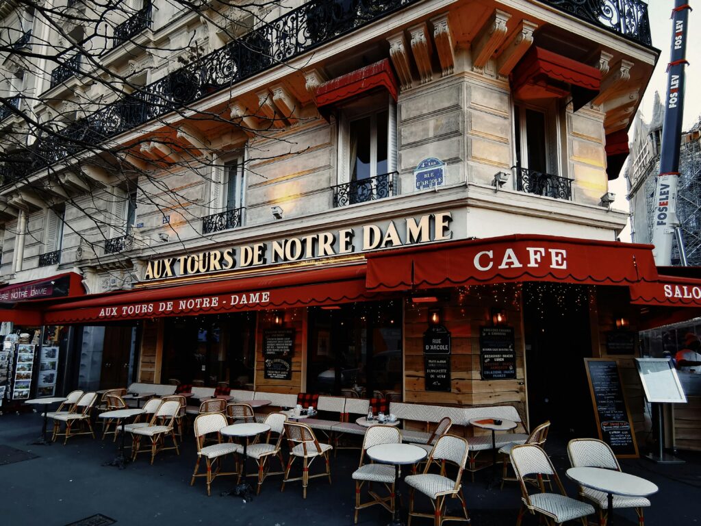 Parisian cafe Aux Tours de Notre Dame with empty outdoor seating in a vibrant urban setting.