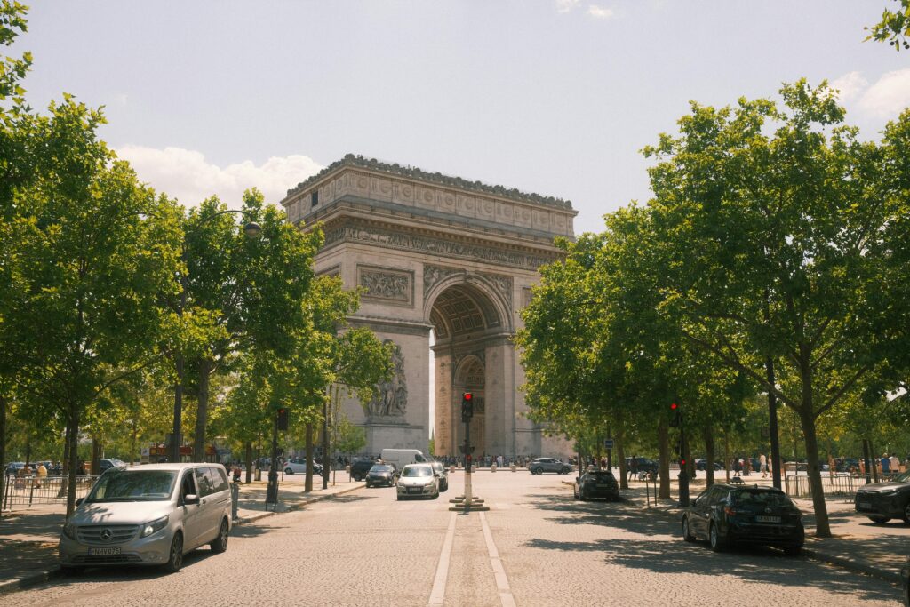View of the iconic Arc de Triomphe in Paris surrounded by trees and traffic on a sunny day.