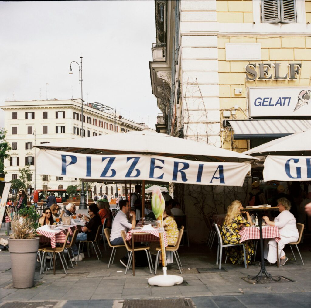 People enjoying a meal outside a pizzeria in Rome, Italy with iconic architecture.