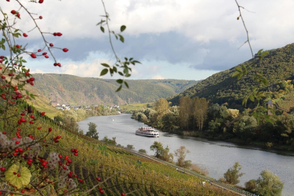 Autumn landscape of Mosel River in Cochem with a ferry navigating through scenic hills.