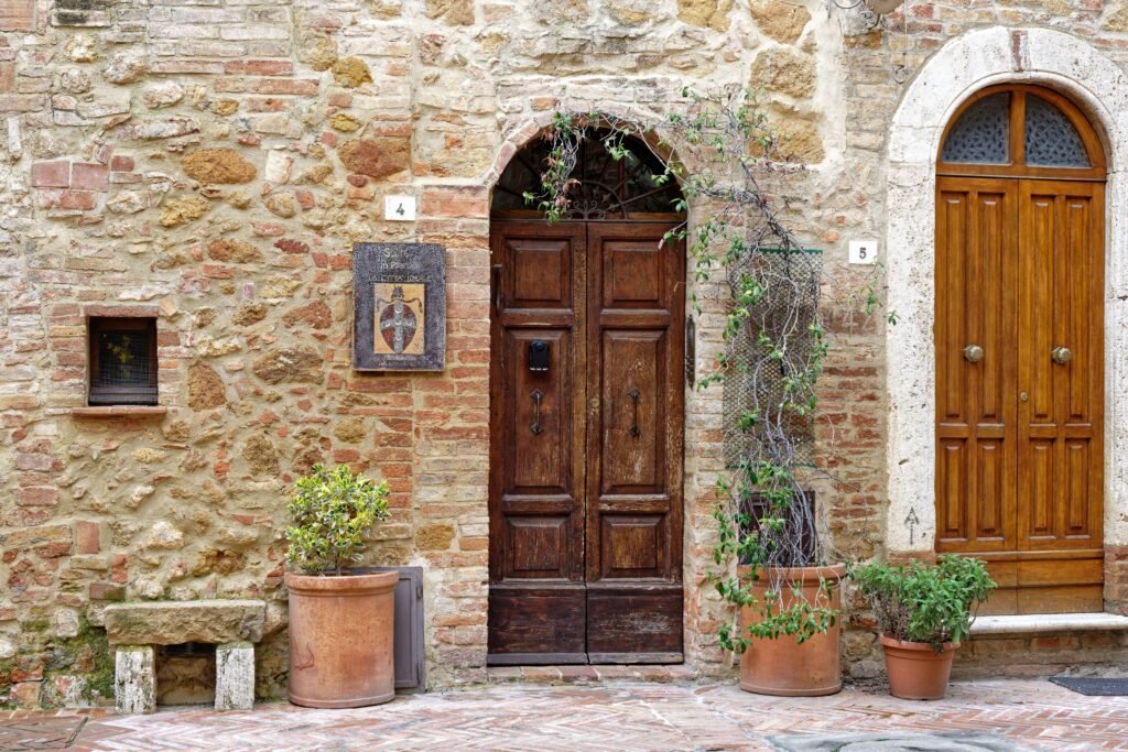 Rustic wooden doors with potted plants on a stone facade in Pienza, Tuscany.