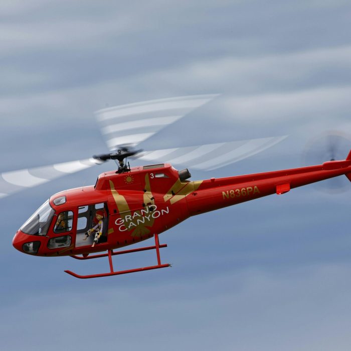 Vivid red helicopter with Grand Canyon branding flying in a clear sky.